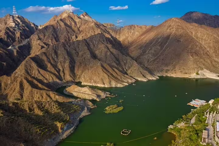 Scenic view of Fujairah's natural landscape featuring a tranquil lake surrounded by rocky mountains under a blue sky.