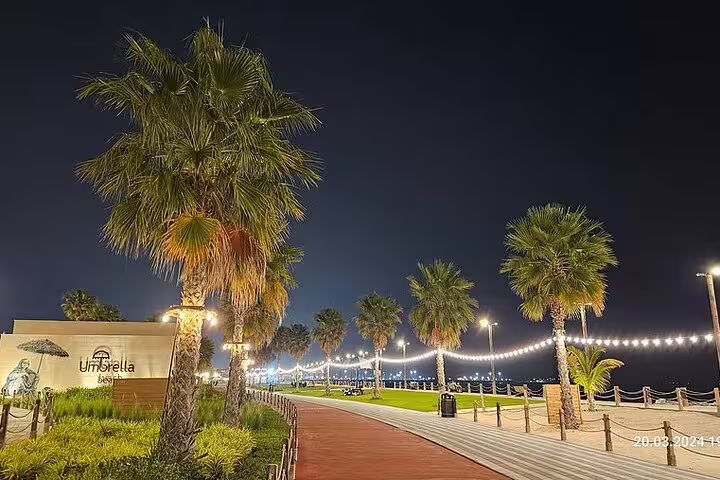 Nighttime view of a palm-lined promenade in Fujairah with ambient lights, ideal for a relaxing heritage tour experience.