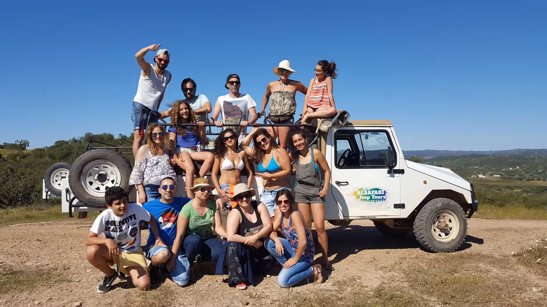 Group of friends posing on a 4x4 jeep during a full day Algarve safari tour under clear blue skies in rural Portugal