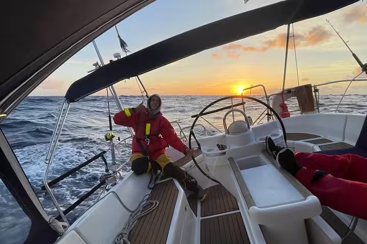 Sailors enjoying a full day private sailing cruise at sunset, navigating the open sea with vibrant skies and ocean waves.