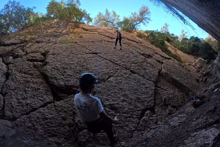 Climbers ascend a rugged rock face surrounded by lush greenery on a full-day adventure trail near Lisbon.