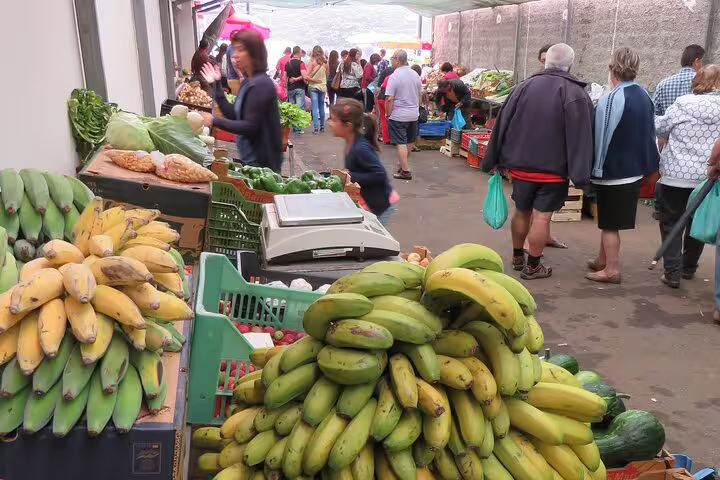 Shoppers explore vibrant local farmers market in Funchal, surrounded by fresh bananas and vegetables, ideal for 4WD tour stops.