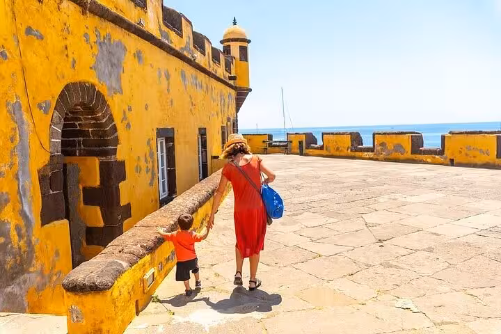 Woman and child explore the vibrant yellow walls of Funchal's historic São Tiago Fort on a sunny day.
