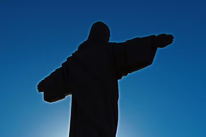 Silhouette of a large statue with outstretched arms against a clear blue sky, highlighting a scenic point near Funchal.