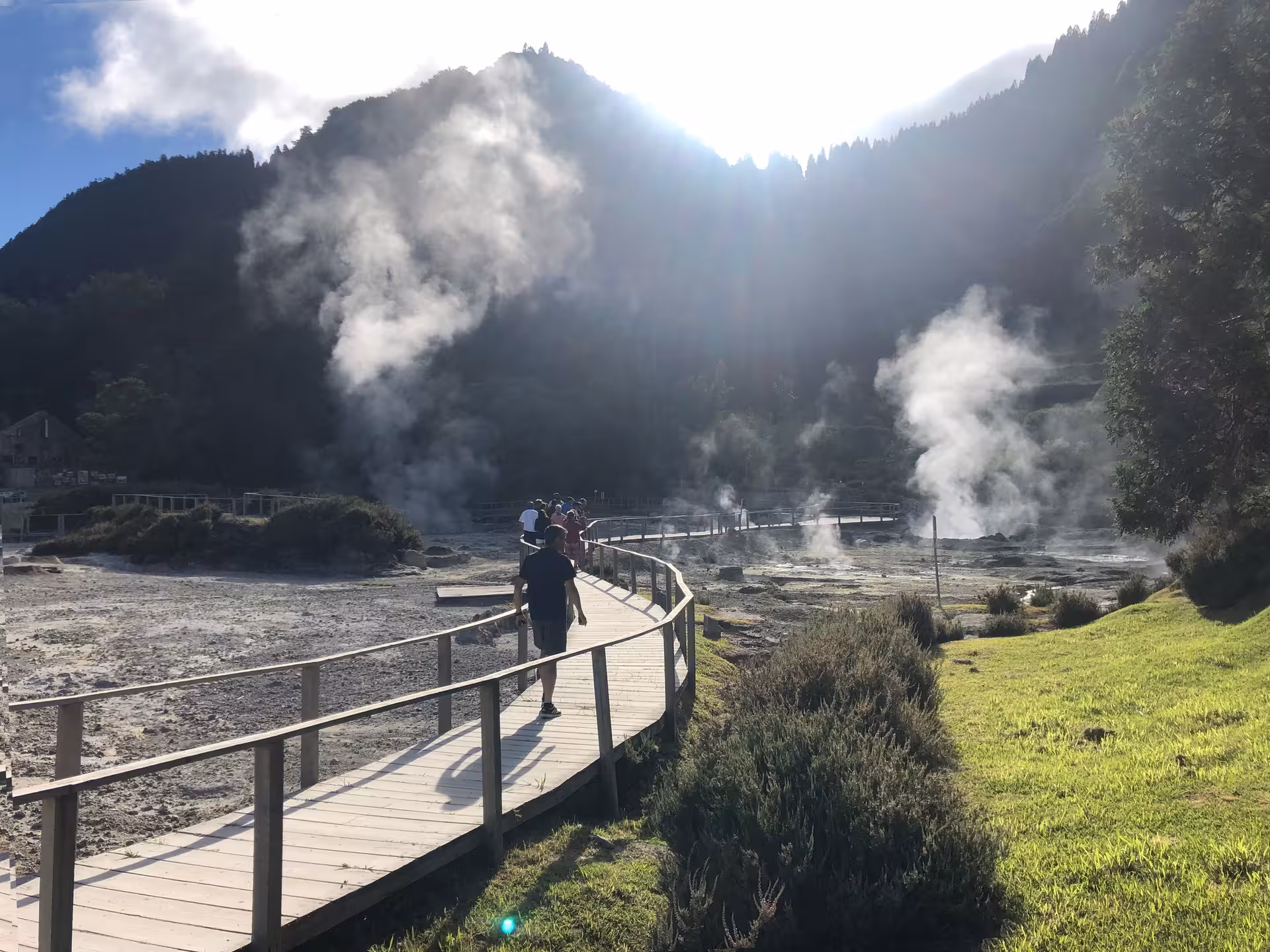 Visitors walking along wooden boardwalk through steaming geothermal fields in Furnas Valley on São Miguel, Azores