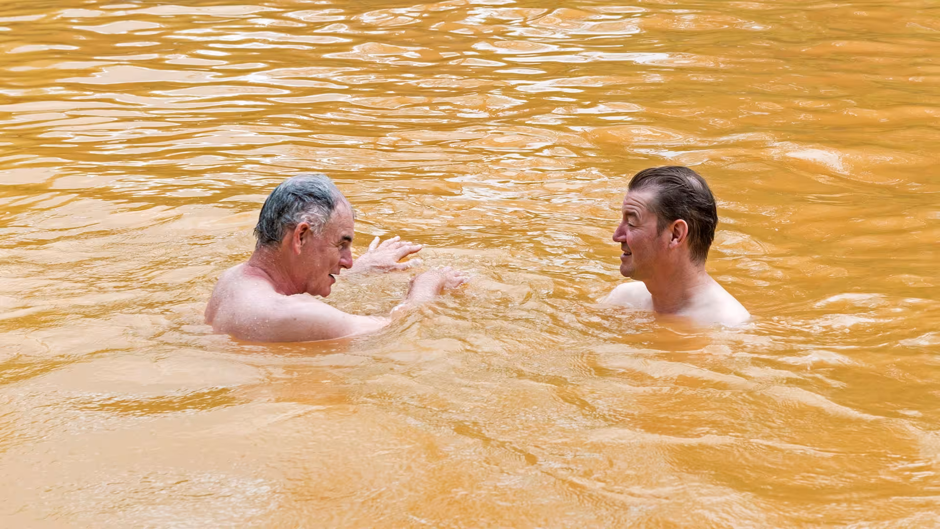 Two visitors relax in the warm iron-rich thermal waters of Furnas hot springs during an Azores wellness experience
