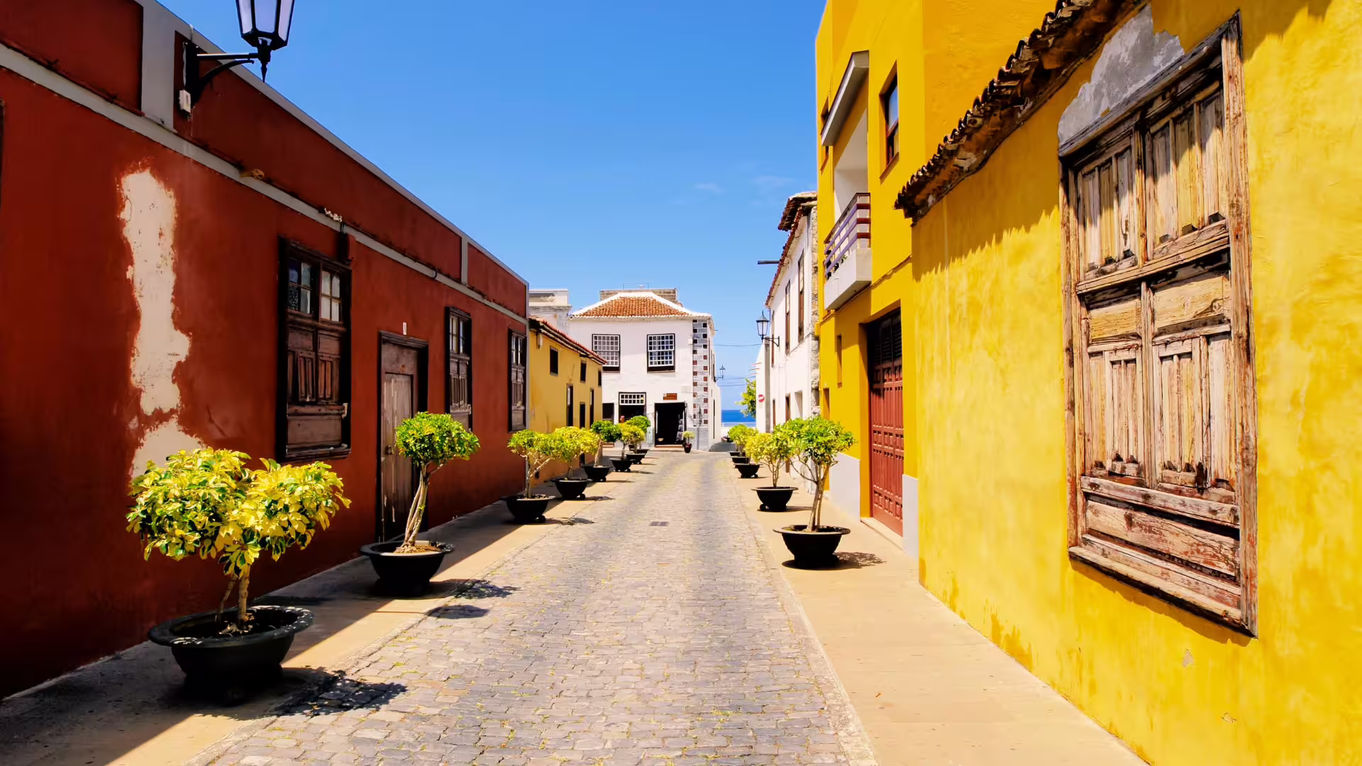 Charming cobblestone street in Garachico lined with colorful buildings and potted plants under a clear blue sky.