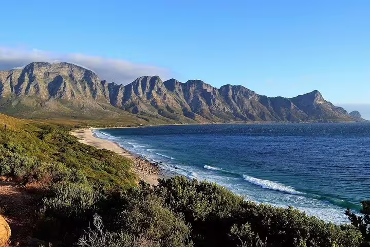 Scenic coastal view of the Garden Route in Africa with mountains, sandy beach, and blue ocean under a clear sky.