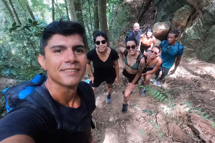 Group of hikers smiling on the Garganta do Céu trail in Pedra da Gávea, surrounded by lush Brazilian rainforest.