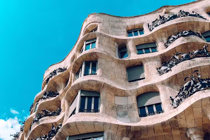 Exterior view of Gaudi's La Pedrera, showcasing its unique wavy stone façade under a clear blue sky.