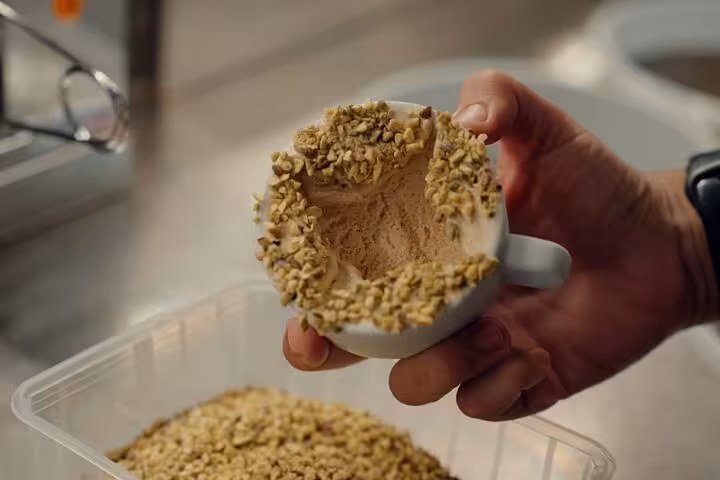 Hand holding a cup dusted with crushed nuts, showcasing a unique gelato creation in Florence's culinary tour.