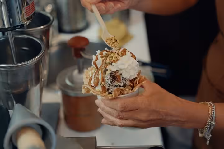 Hand crafting a delicious gelato sundae with toppings at a Florence gelato shop, perfect for a culinary walking tour.
