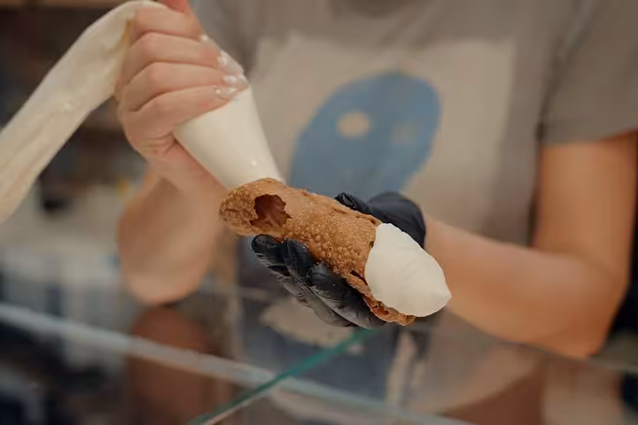 Person filling a cannoli shell with creamy gelato, highlighting hands-on experience in Florence gelato tour.