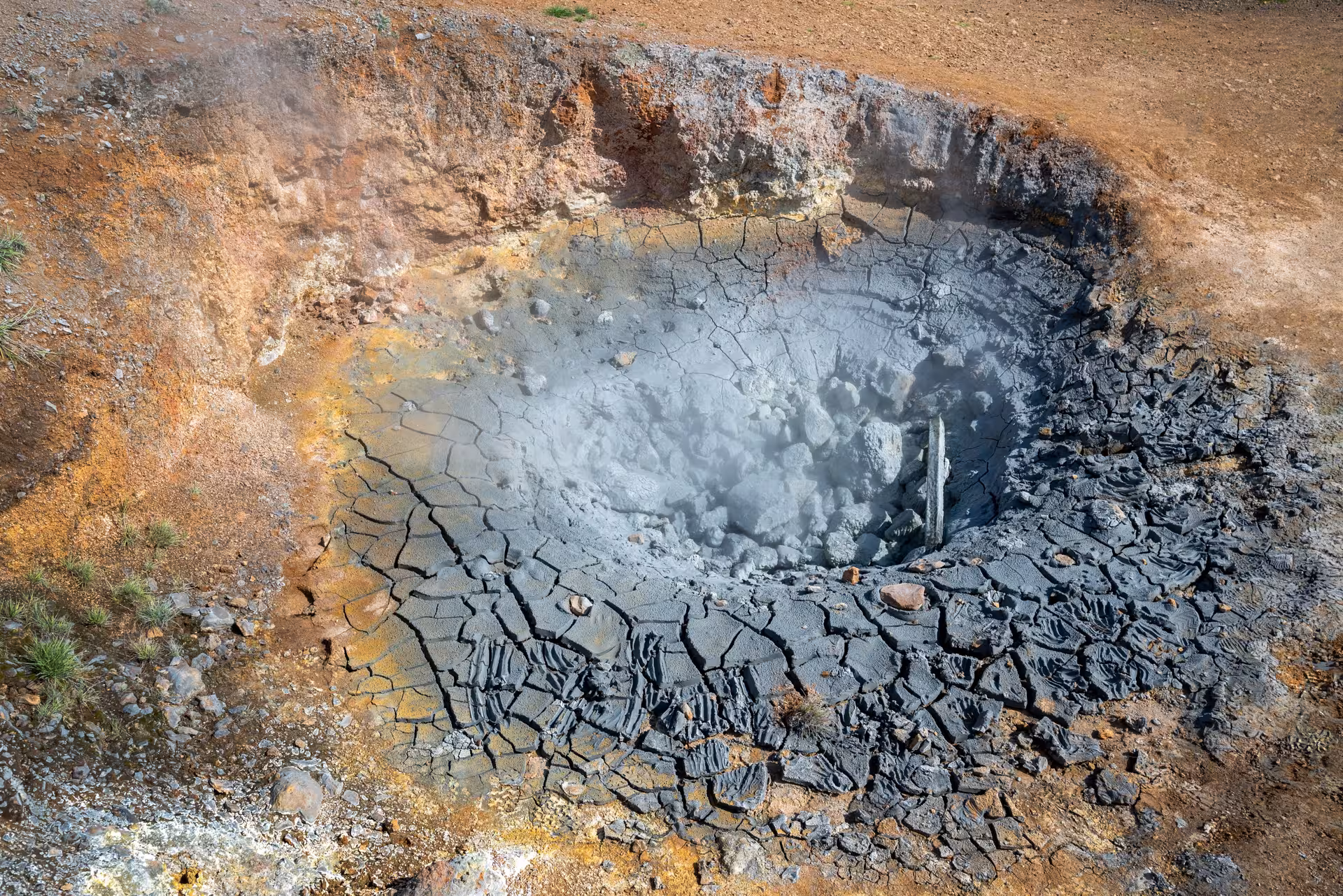 Steaming geothermal mud pot with cracked clay in Grændalur valley, stop on private Reykjadalur circle hike tour