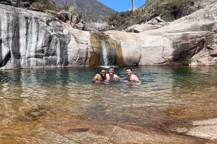 Visitors swimming in a refreshing natural lagoon at Geres National Park, surrounded by stunning rock formations and waterfalls.