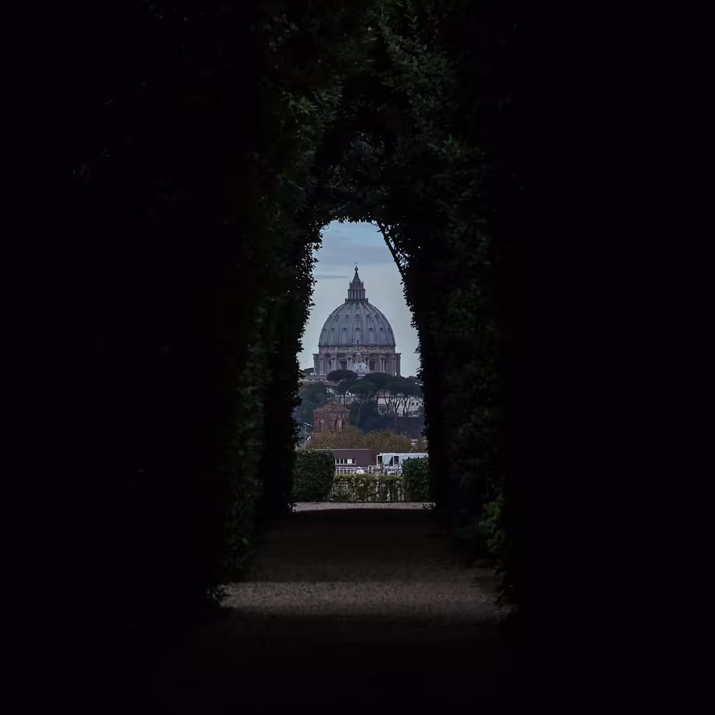 Dark hedge tunnel framing a distant dome in Rome at dusk, hinting at hidden views on a Ghosts of Rome night tour