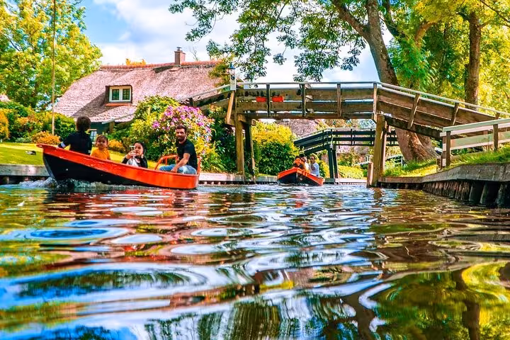 Private boat tour in Giethoorn canal under wooden bridge, passing thatched cottages and gardens