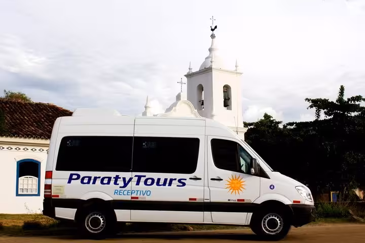 Paraty Tours shuttle parked near a historic church, providing exclusive transfers to Rio de Janeiro South hotels.