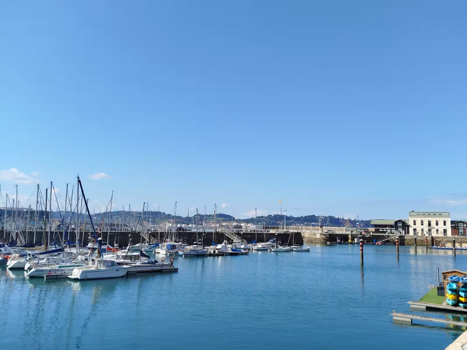 Serene view of boats docked at Gijon's harbor, reflecting the city's maritime charm on a sunny day.
