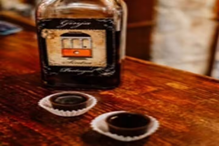 Bottle of traditional Ginja liqueur with chocolate cups on a wooden table, featured in Lisbon's historic half-day tour.