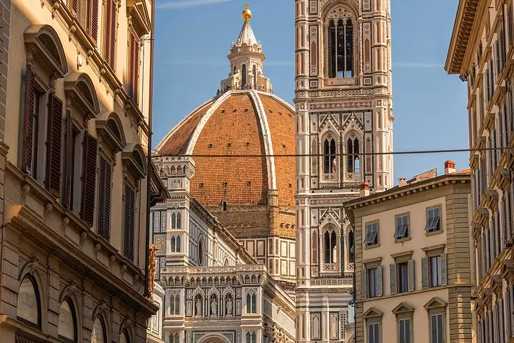 Giotto's Bell Tower and the iconic dome of Florence Cathedral framed by historic buildings on a sunny day.