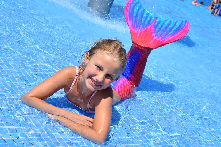Girl with a colorful mermaid tail poses in a Hersonissos pool for a unique photoshoot experience.