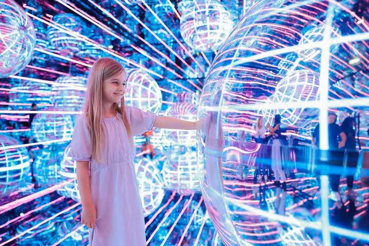 Young girl explores vibrant neon light spheres at Aya Universe, Dubai's immersive videography tour attraction.