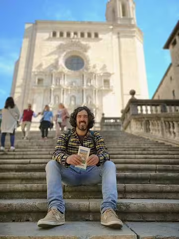 A visitor sits on historic stone steps in front of a grand medieval cathedral in Catalonia during a guided day trip.