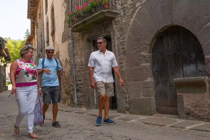 Tourists explore a charming medieval village in Catalonia, walking along cobblestone streets surrounded by historic stone buildings.