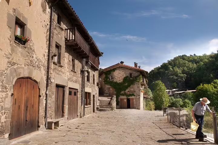 Charming medieval village street in Catalonia with rustic stone buildings, lush greenery, and a serene atmosphere under blue skies.