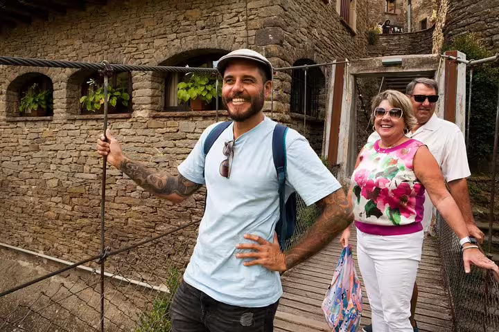 Tourists enjoying a charming medieval village tour in Catalonia, crossing a rustic bridge surrounded by historic stone architecture.