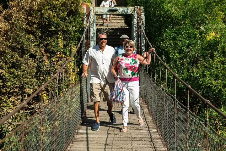 Tourists enjoy a scenic walk on a rustic bridge during a private full-day trip to medieval villages in Catalonia with lakefront lunch.