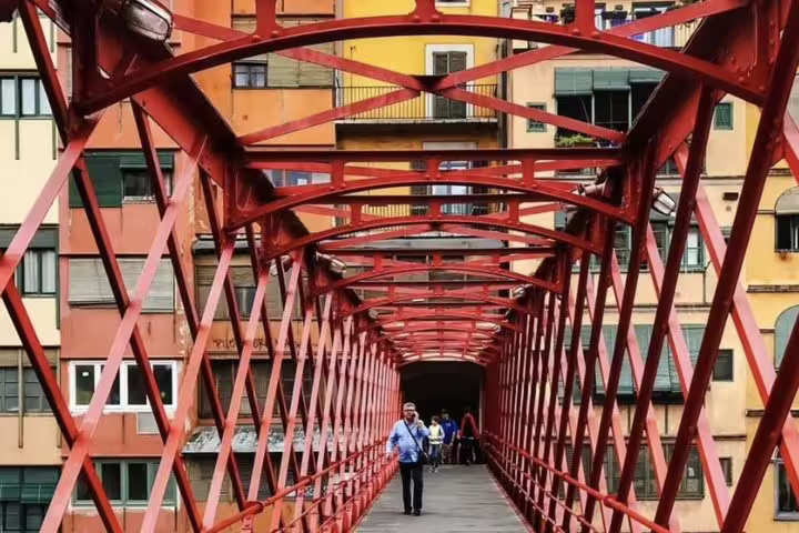 Tourists walking on the iconic red bridge in Girona with colorful buildings in the background, part of a private tour.