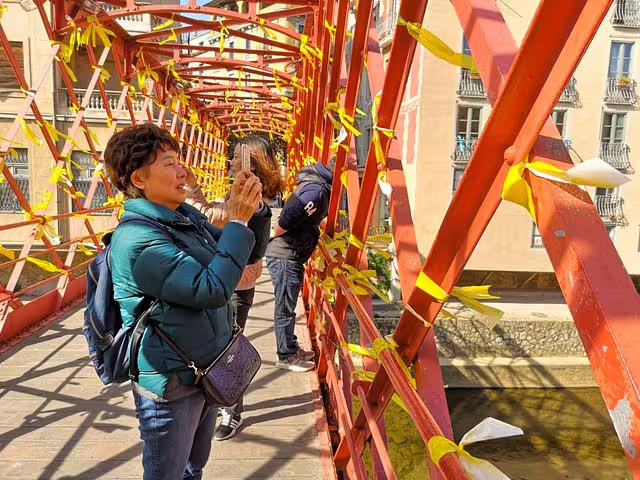 Tourists capture photos on the iconic red iron bridge in Girona, Catalonia, during a private medieval village day trip.
