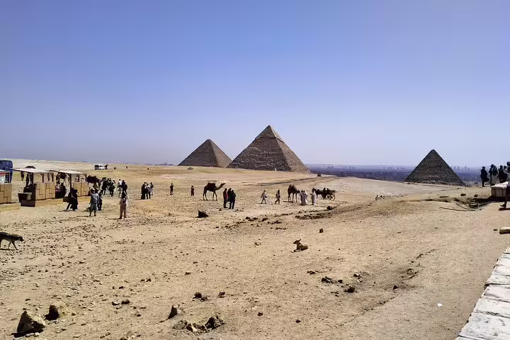 Giza Pyramids plateau with visitors and camels under clear sky, Cairo stop on 8-day Egypt pyramids cruise tour