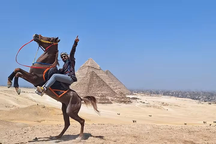 Tourist riding a rearing horse with Giza Pyramids in the background on a private adventure tour with camel ride.