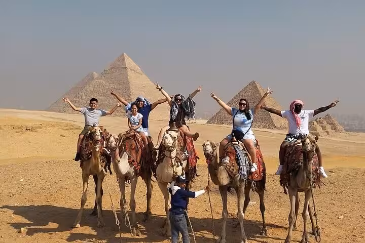 Group of tourists enjoy a camel ride in front of the Giza Pyramids, part of a private tour with Sphinx, Memphis, and Saqqara.