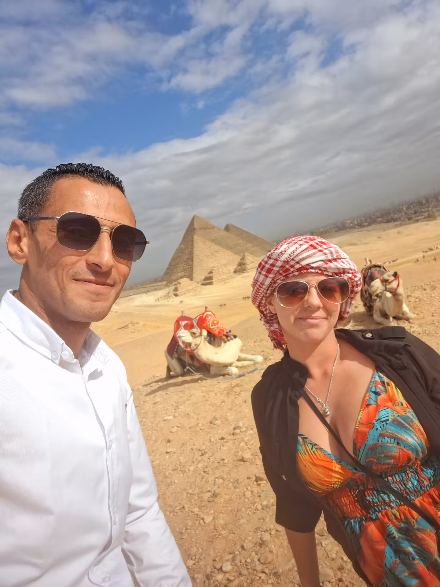 Tourists enjoy a sunny day at the Giza Pyramids with camels in the background on the Egypt Golden 15 Days tour.