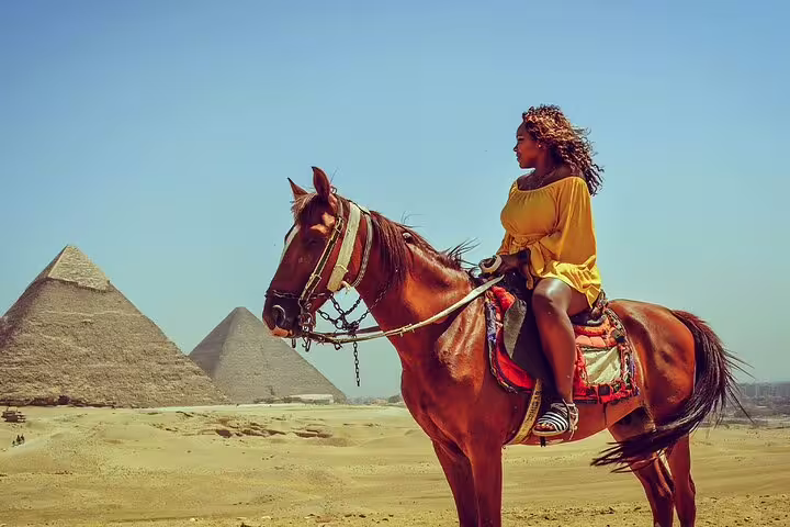 Traveler riding a horse with Giza Pyramids in the background, scenic half-day tour in Cairo desert
