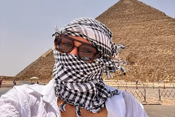 Tourist in keffiyeh with the Great Pyramid of Giza behind, part of a Giza Pyramids Saqqara Memphis day trip