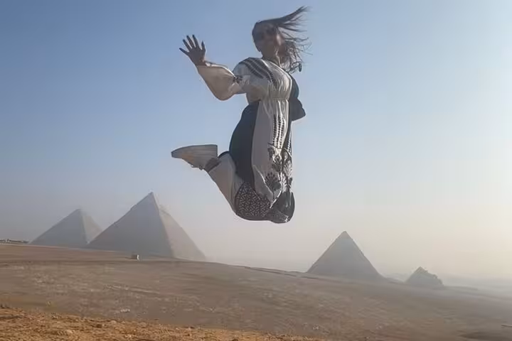 Traveler jumps with Giza Pyramids backdrop on private tour with camel ride and lunch in Cairo, Egypt