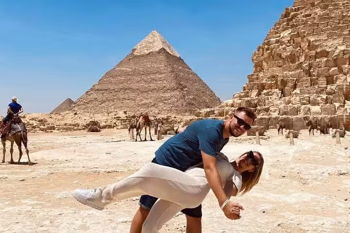 Couple photo at Giza Pyramids near ancient stone blocks, private Cairo tour with camel rides and desert views