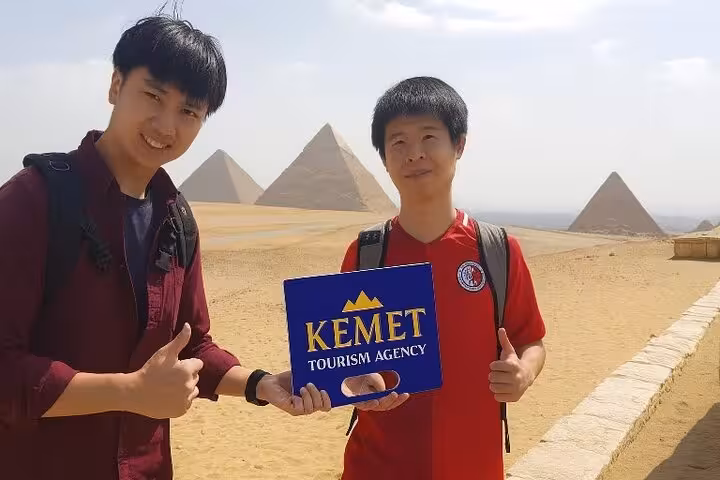 Guests holding Kemet sign with Giza Pyramids backdrop on half-day private tour with expert Egyptologist guide