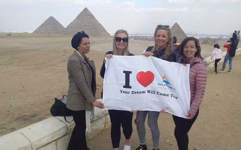 Tour group photo with banner at the Giza Pyramids viewpoint, Cairo, on a full-day pyramids excursion