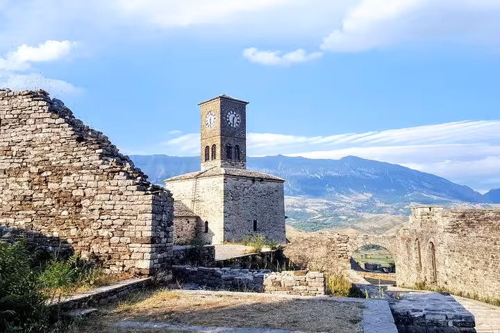 Discover the historic Gjirokastër Castle with its iconic clock tower against a backdrop of stunning Albanian mountains.