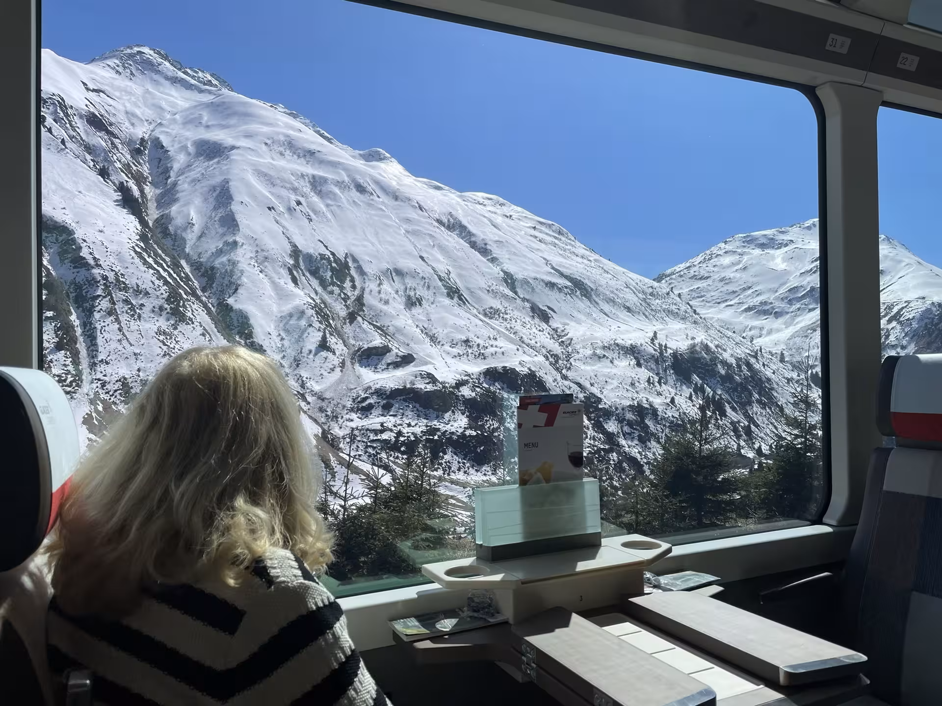 Passenger enjoying panoramic Glacier Express window views of snow-covered Swiss Alps on private Zurich rail tour