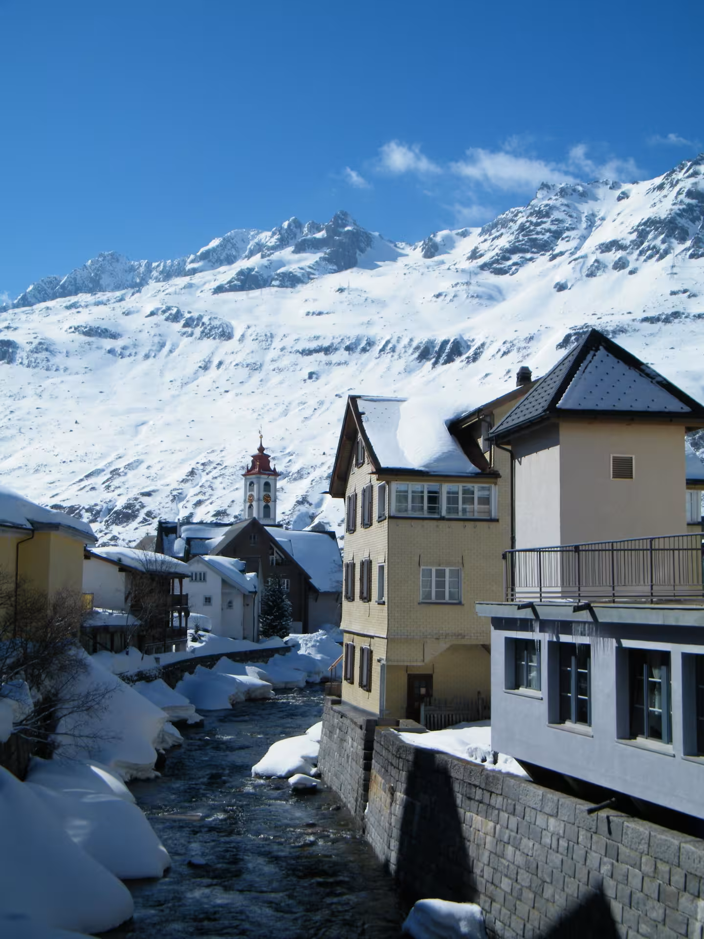 Snowy Swiss village and stream beneath Alps on Premium Glacier Express route tour from Zurich, winter view