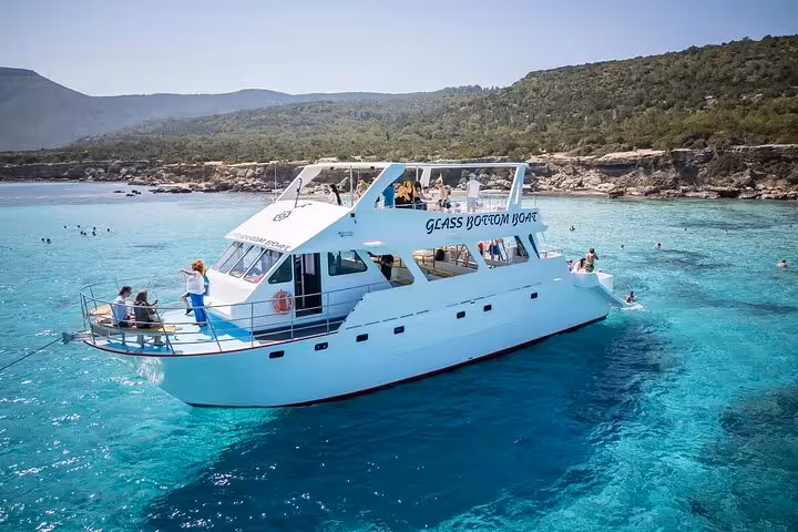 Glass-bottom boat anchored in Blue Lagoon Akamas with swimmers, part of the Paphos bus and boat tour with slide