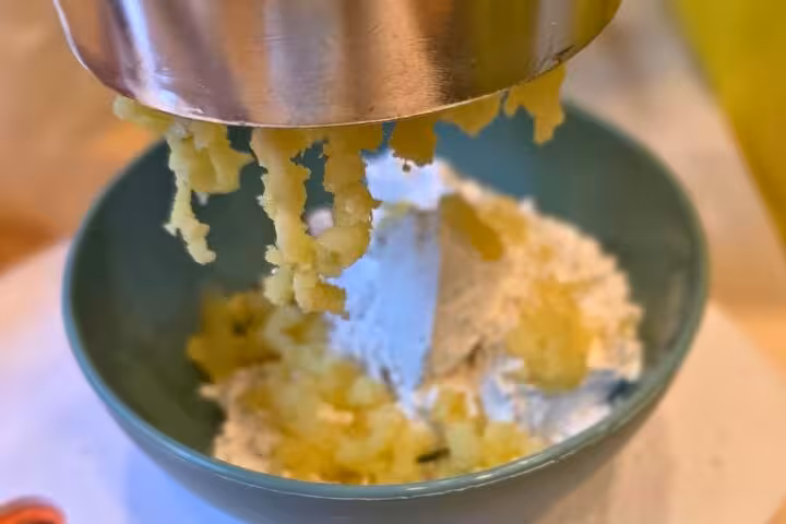 Potatoes being riced over flour for gluten-free gnocchi in Chef Christian's Roman feast class.
