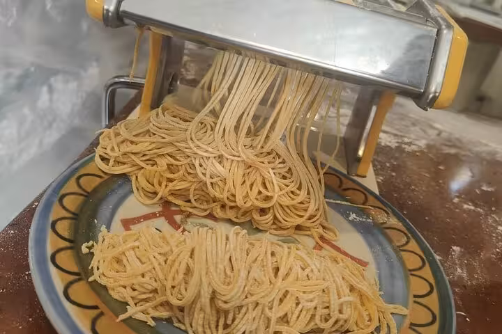 Fresh gluten-free spaghetti emerging from a pasta machine during a culinary class in Rome.